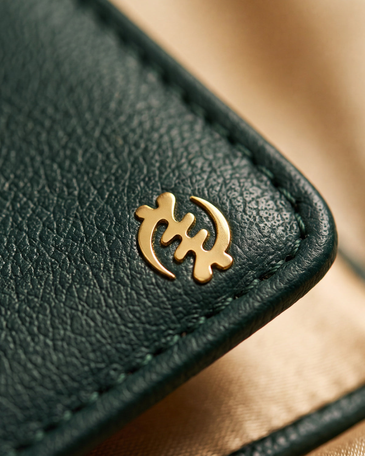 Close-up of green leather with a gold Gye Nyame Adinkra symbol
